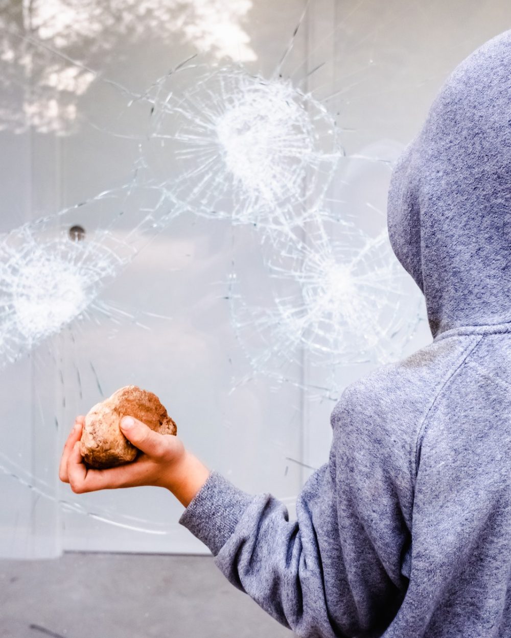 Protester holding a rock to break the glass of a shop window in the street during protests. Protester holding a rock to break the glass of a shop window in the street during protests.